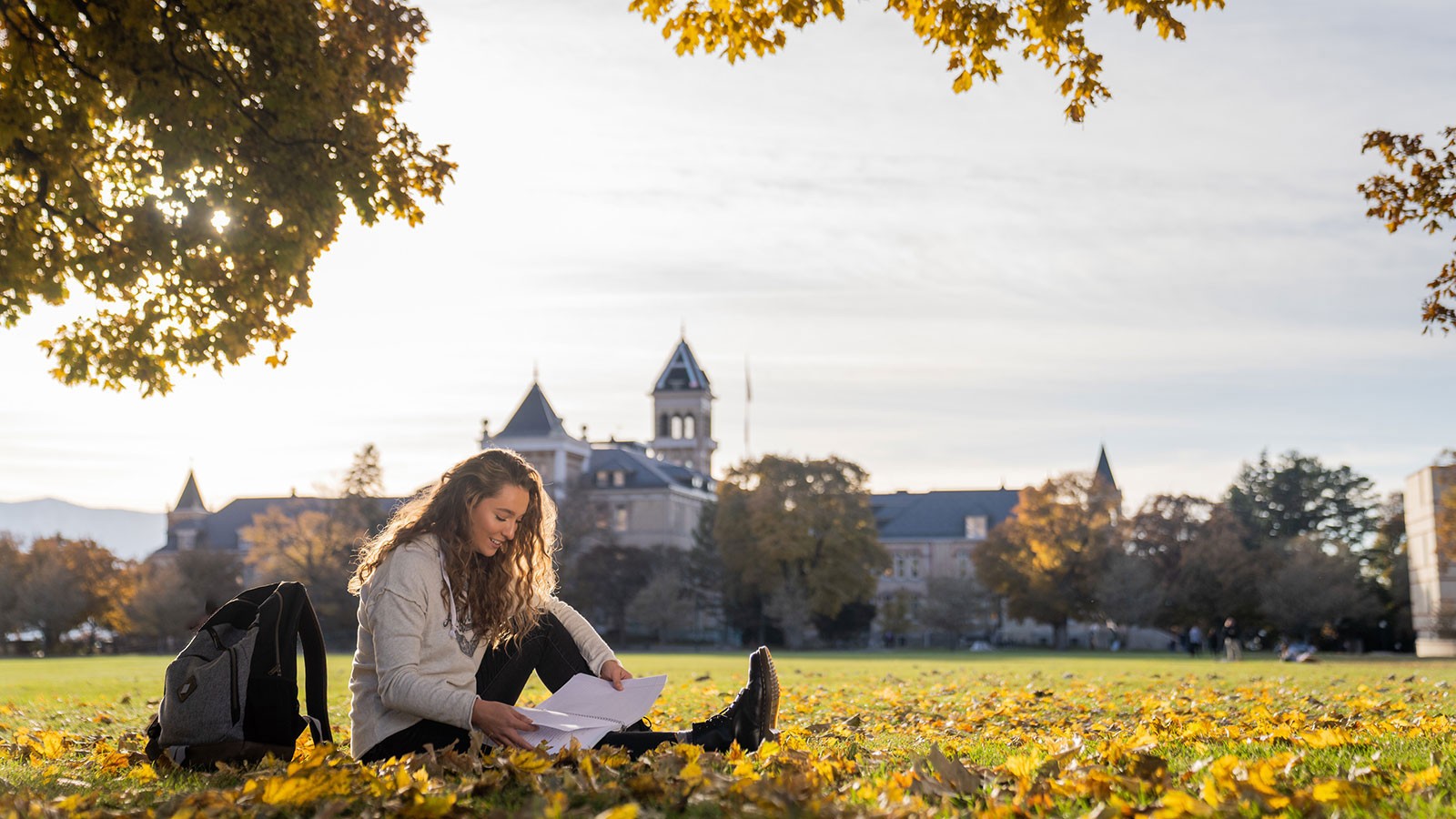 student sitting in the leaves on USU's Quad.