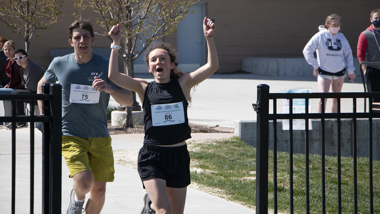 Two people in athletic wear run through a gate.