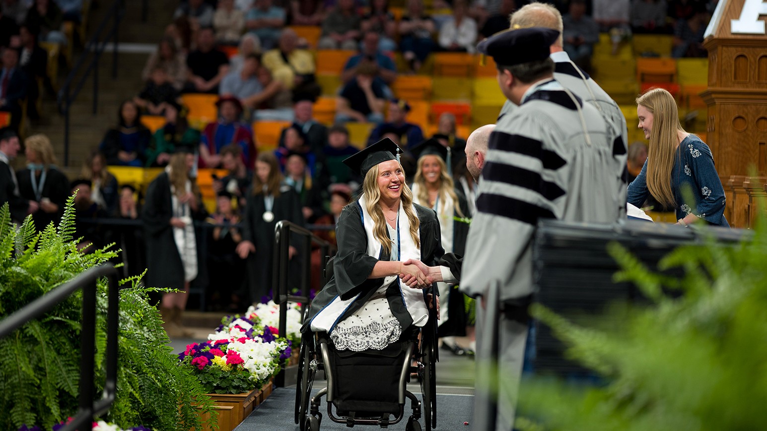 A woman in graduation regalia crosses the graduation stage.