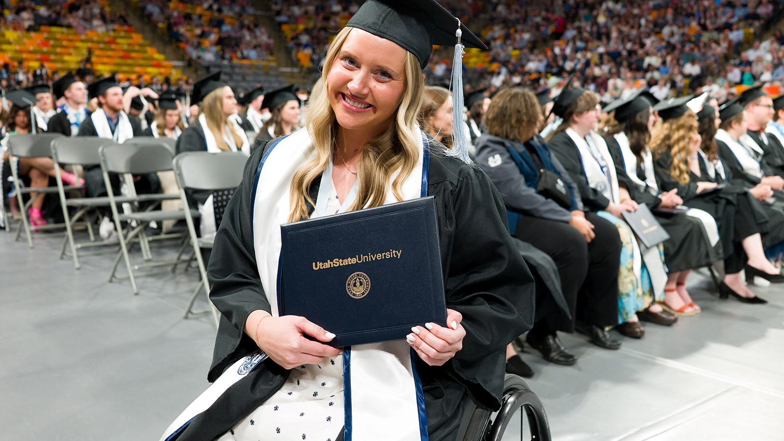 A woman in a wheelchair poses for a photo in graduation regalia.