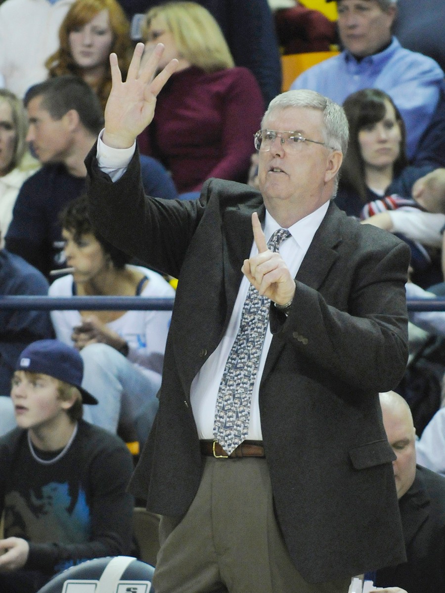 A basketball coach makes a hand signal to players during a basketball game.