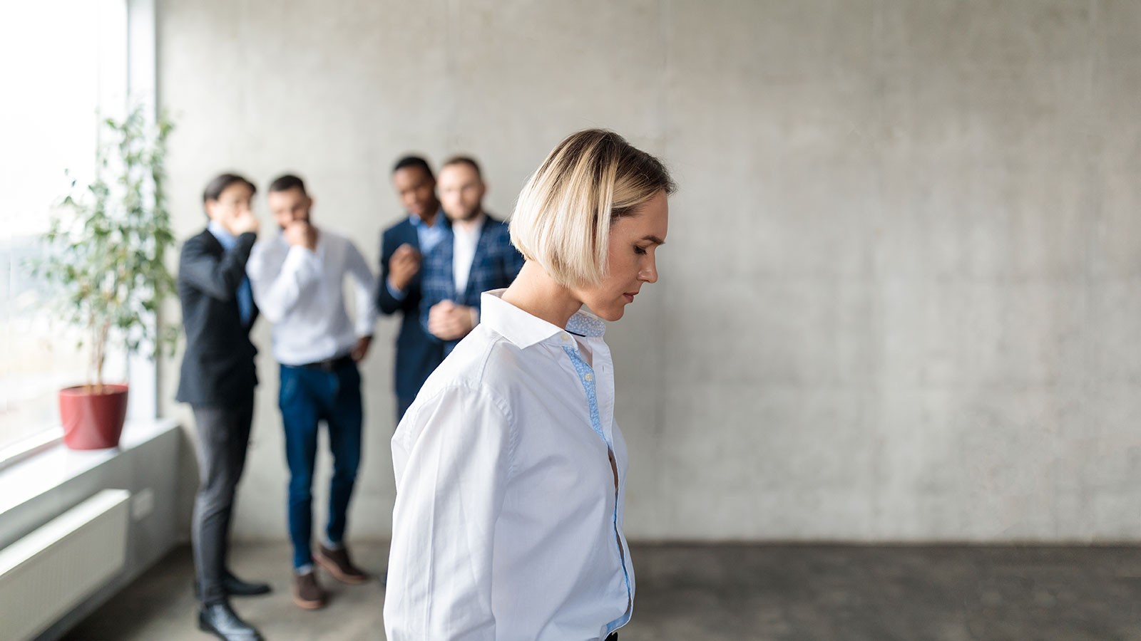 A woman hangs her head as men in the background look at her and laugh to themselves.