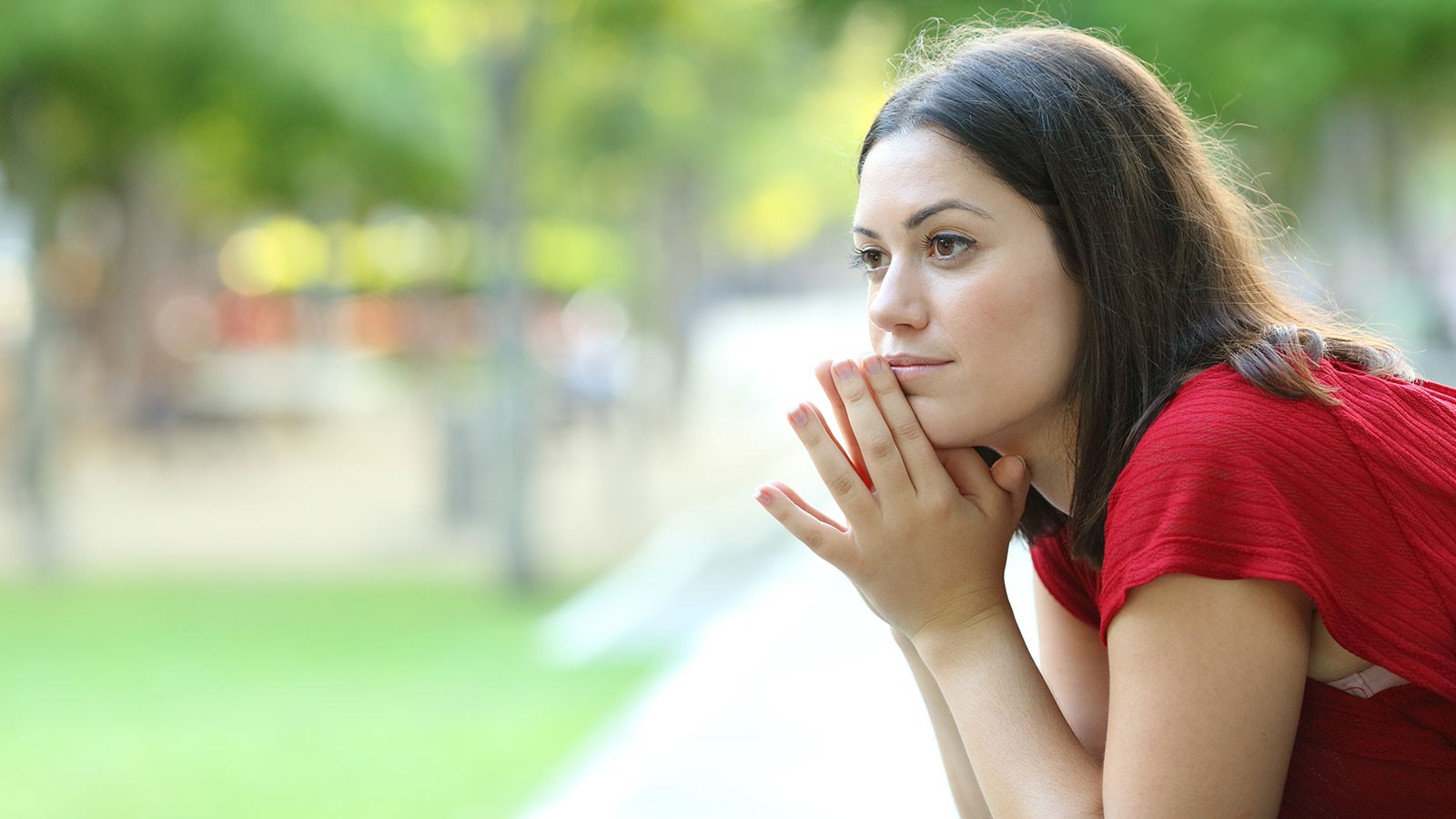 A woman sits in a thinking posture in a park.