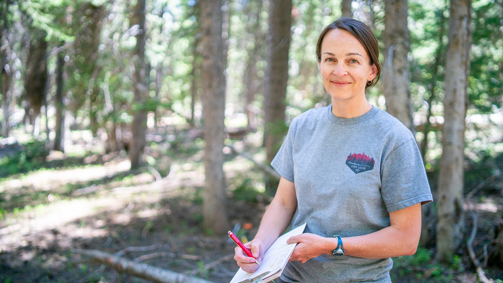 Larissa Yocom stands with a clipboard in the forest while conducting field work.