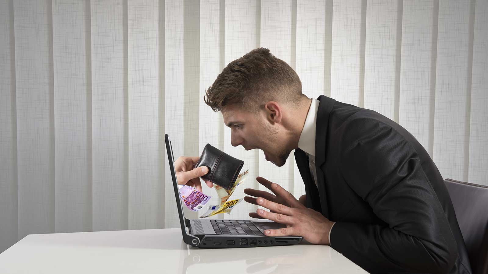 person sitting at a computer and holding a wallet.