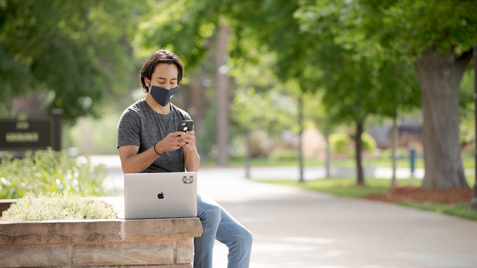 student wearing a mask and sitting next to a laptop.
