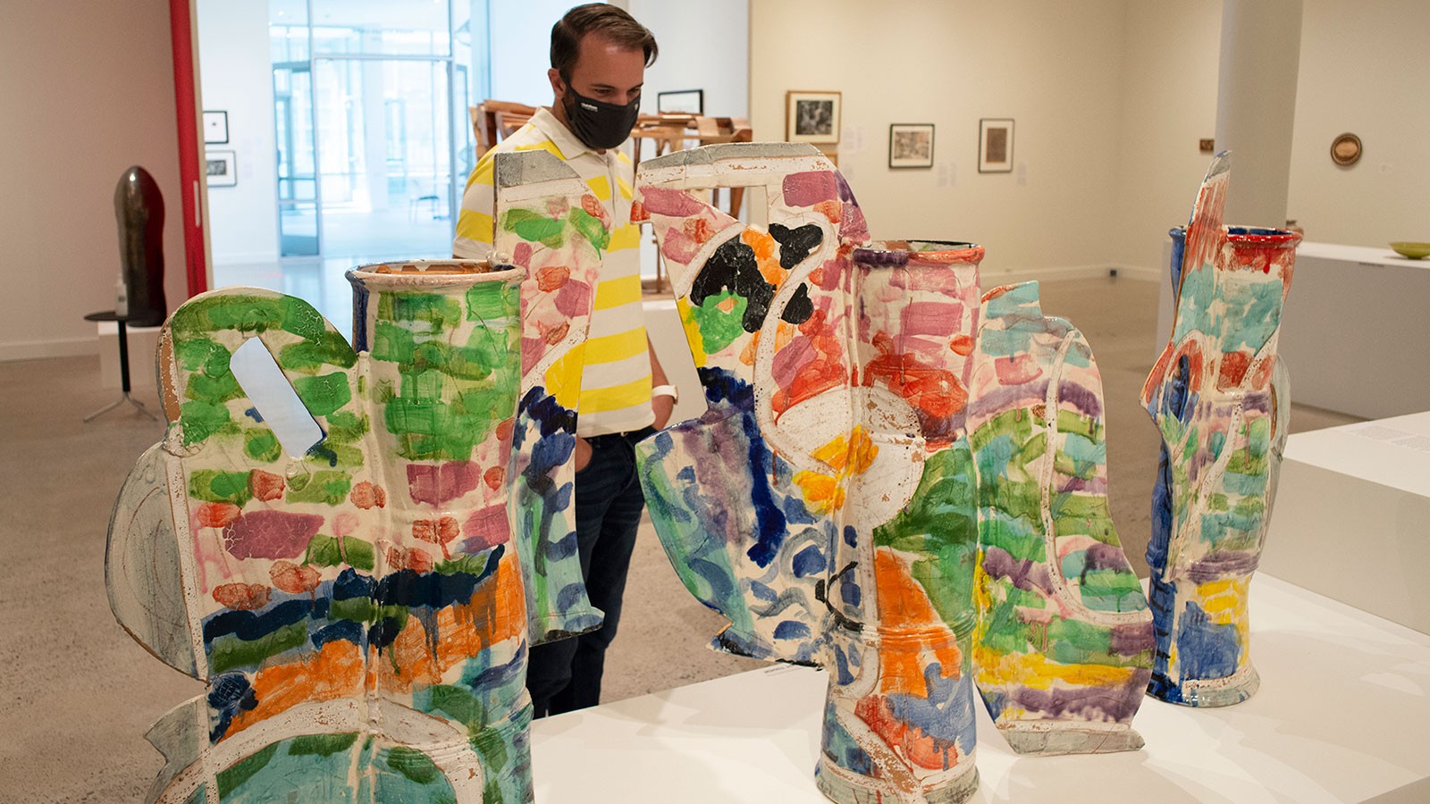 A man studies multicolored, pottery-like sculptures.