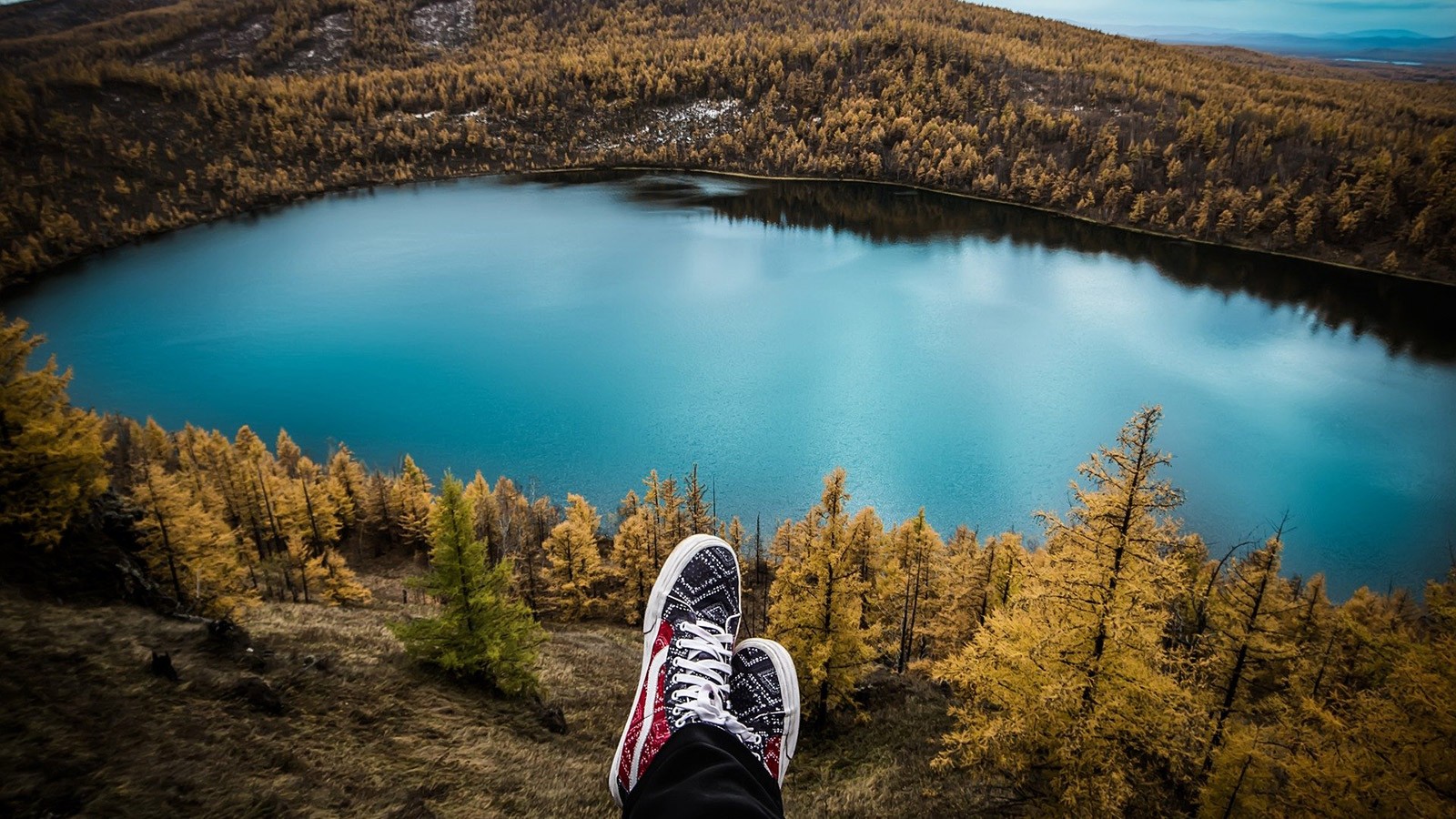 person's shoes shown overlooking a mountain lake vista.
