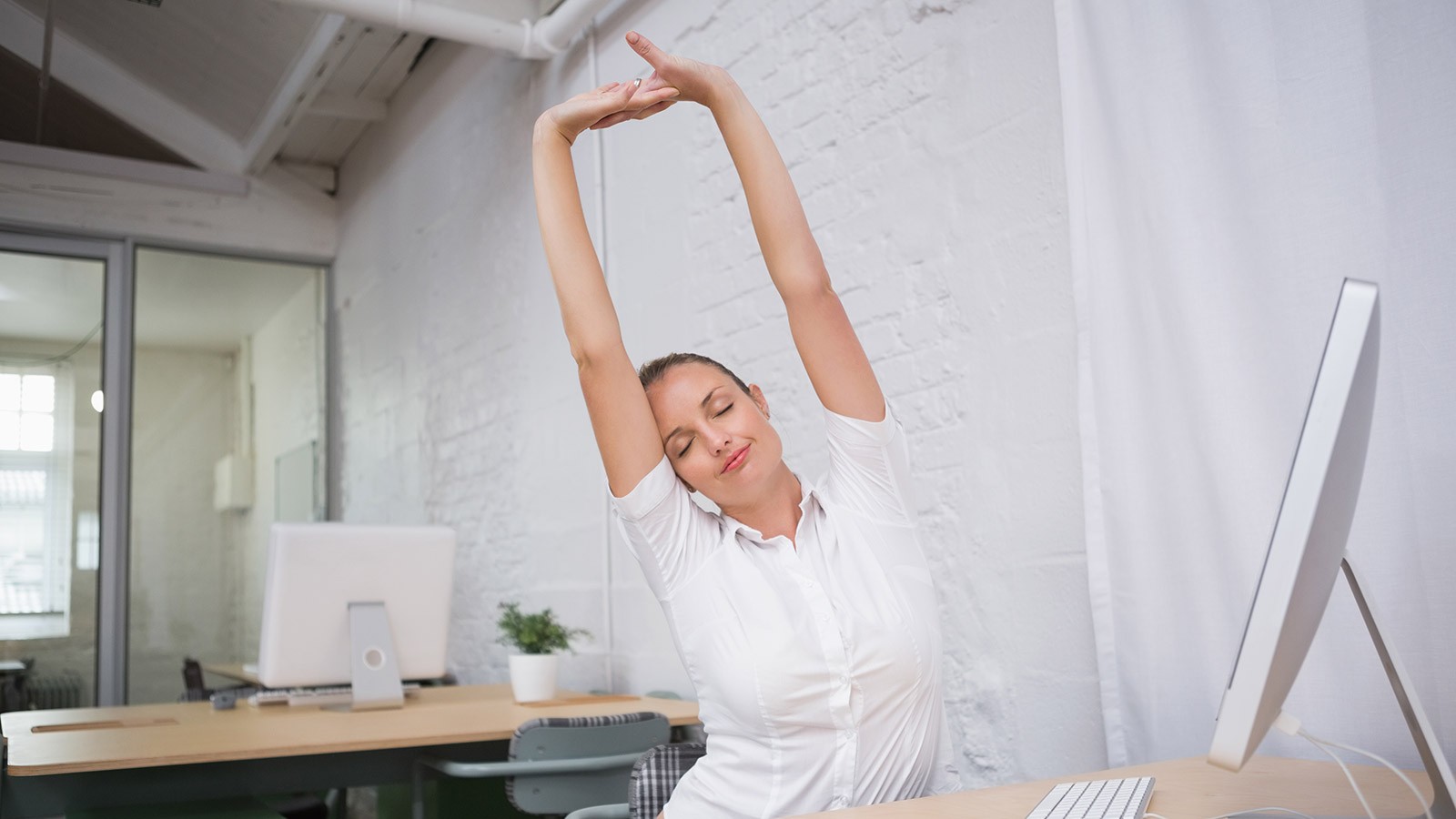 woman stretching while sitting at a desk.